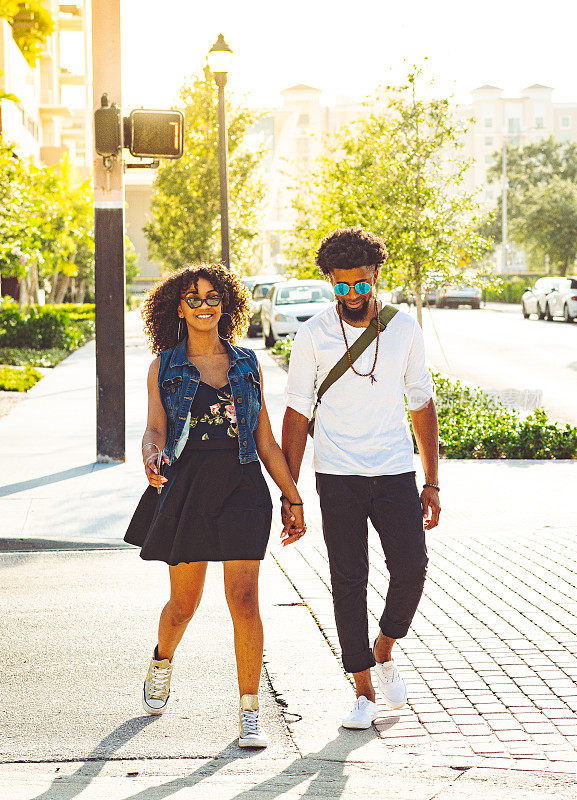 迷人幸福的黑人情侣手牵着手过马路，夏天的城市