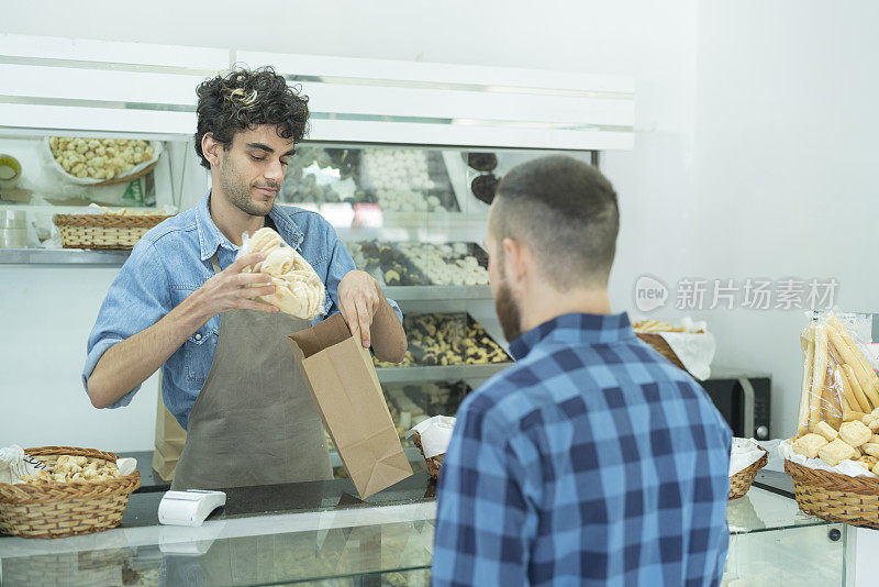 面包房的年轻男员工把一条面包放在纸袋上