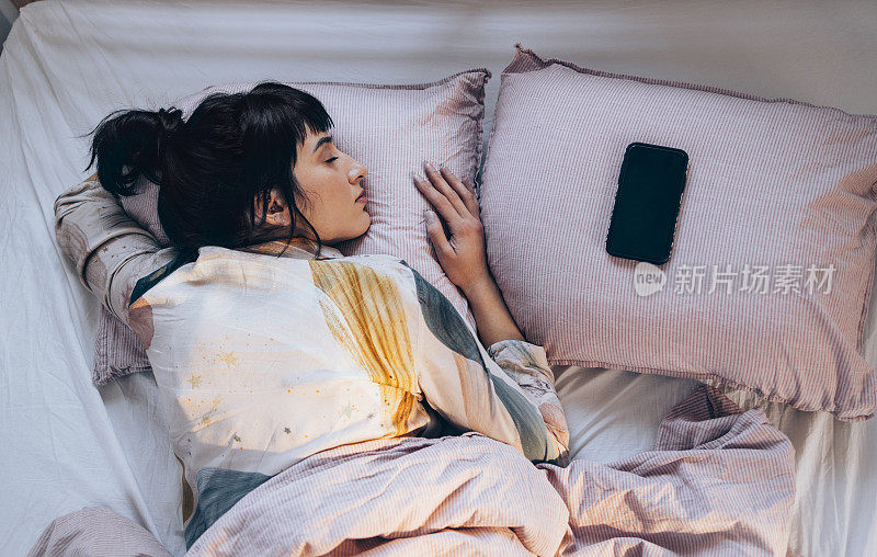 科技辅助睡眠:女人早上躺在床上用智能手机听放松的音乐