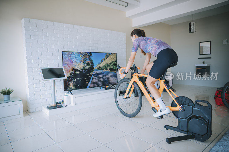 亚洲中国妇女骑自行车与固定自行车教练在家里