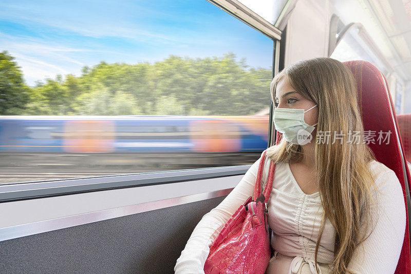年轻的乘客面具金发女人在火车上看着窗户在英国