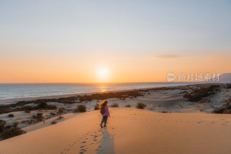 在土耳其海边的沙丘上，背着背包的女人凝视着风景优美的日落