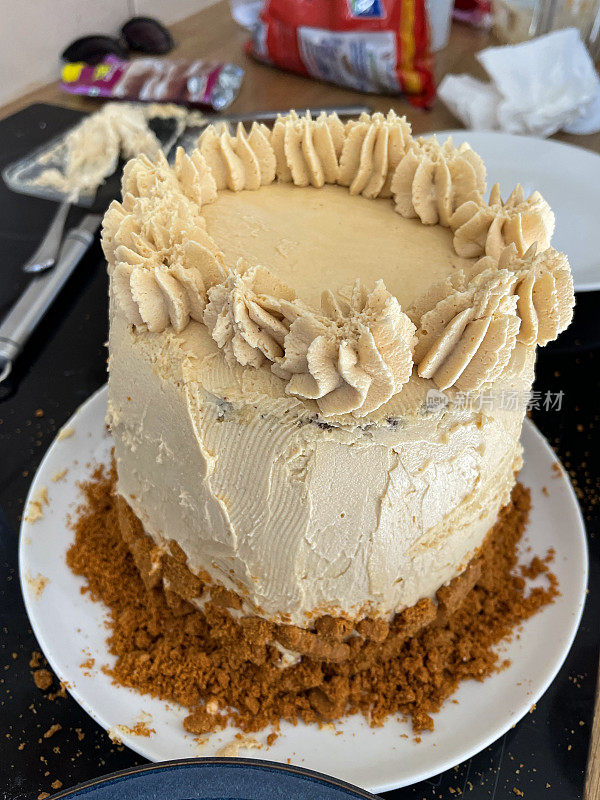 自制的特写图像，巧克力海绵生日蛋糕在白色的盘子，四层庆祝蛋糕覆盖在黄油奶油与管道玫瑰结顶部，饼干屑基础，重点在前景