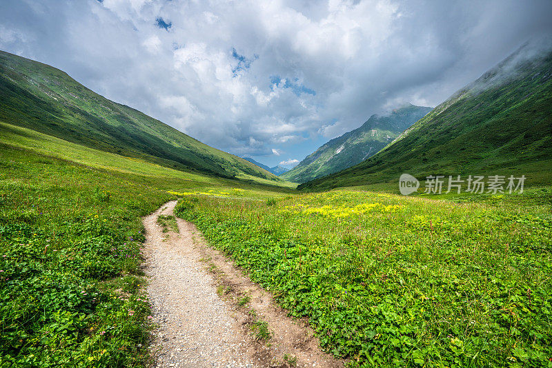 在阳光明媚的日子里，登山驿站在山上，美丽的群山四周被绿色的草和花覆盖着