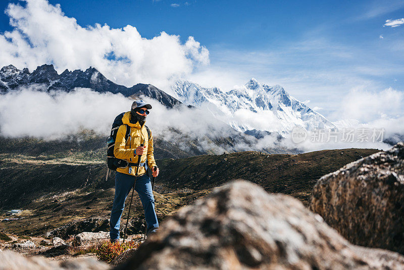 年轻人户外旅行者走在巨大的阳光多云的山路上。背着双肩包，拄着登山杖穿越山路的游客