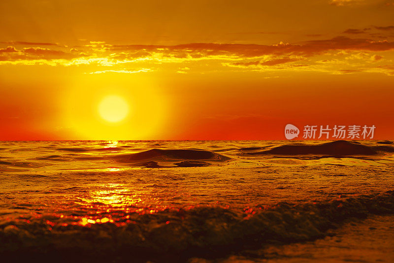 太阳正在沉入大海。阳光穿过波浪，平滑地滚到岸边。海面上橙黄色的落日真是美极了。浪漫暑假的概念。