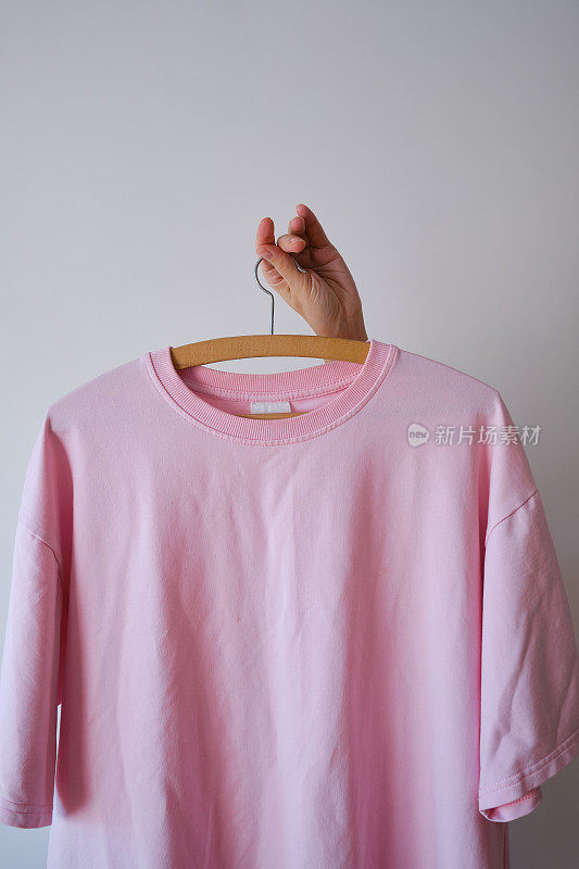 粉色t恤挂在衣架上，浅色背景。拷贝空间。衣架上的衣服