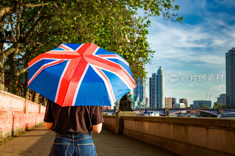 在伦敦市中心的泰晤士河堤上，一名女子手持英国国旗伞