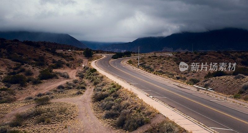 在一个黑暗多云的日子里，一条穿越沙漠的道路以山脉为背景的史诗般的镜头。