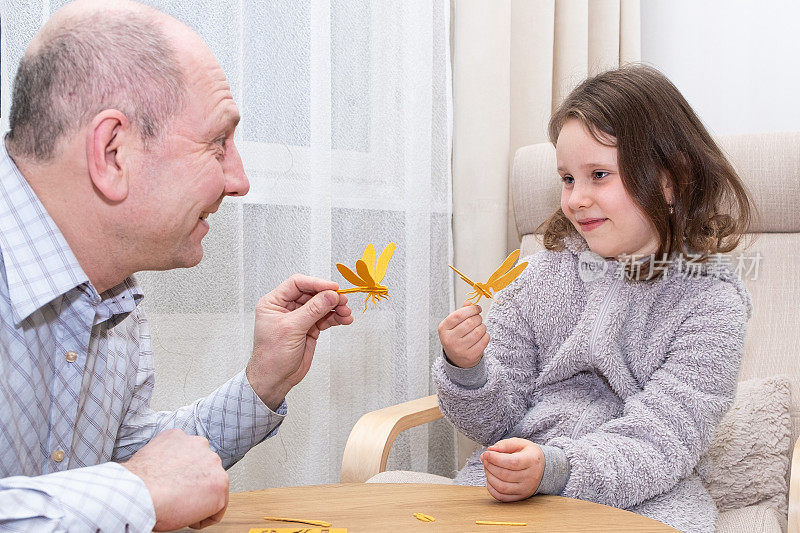一个白人男子和一个7岁的女孩，用木制材料制作蜻蜓玩具。