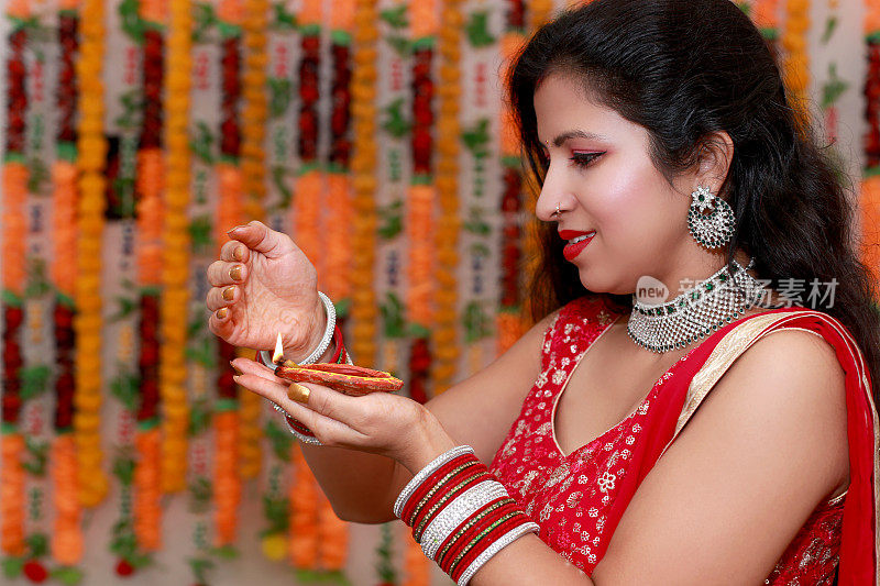 年轻的印度妇女手持油灯，以花卉为背景