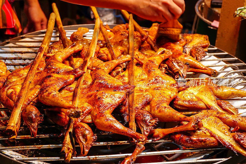 用竹签在炉子上用木炭烤鸡翅，卖主用手把酱汁刷在鸡上。烤鸡烧烤特写。美味的亚洲料理。