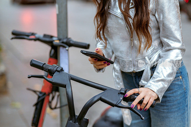 一名女子用智能手机在街上租了一辆电动摩托车。城市生活中的现代交通理念。