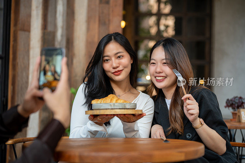 两个美丽的年轻亚洲女性被她的朋友在咖啡馆闲逛时拍照。