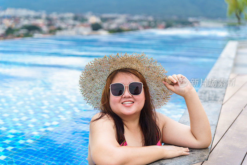 年轻的亚洲女子穿着橙色swimsuitÂ和稻草沙滩太阳帽在游泳池放松快乐加码女人愉快有趣的假期旅行在夏天。