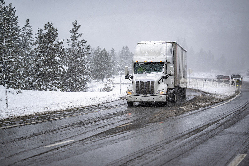 高驾驶室长途车白色大钻机半挂车运输货物的干式厢式半挂车缓慢行驶在冬季潮湿的冰雪公路上