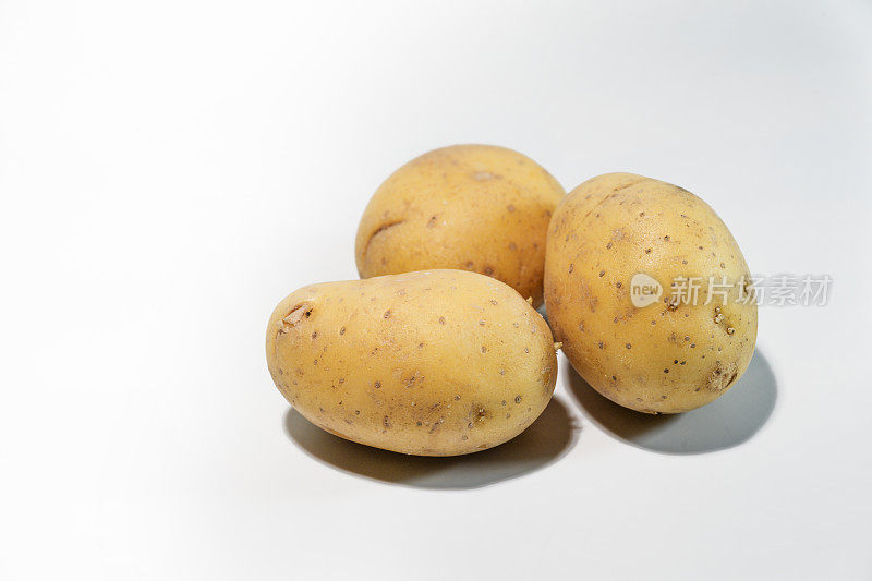 浅灰色背景上的三个生土豆，含碳水化合物的根茎类蔬菜和世界许多地方的主食，复制空间，精选焦点