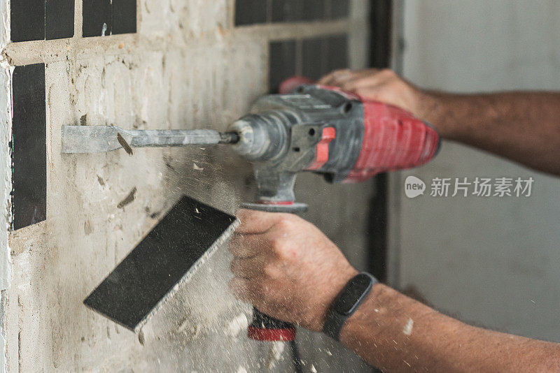建筑工用打孔机拆除混凝土墙上的旧瓷砖