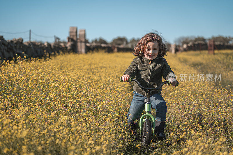 阳光明媚，蓝天明媚，一个快乐的小男孩在黄花草地上玩自行车