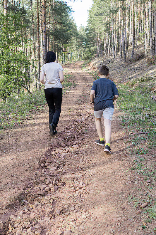 快乐的母子在森林里跑步和锻炼。他们在外面伸伸懒腰，一起享受。运动的生活方式。