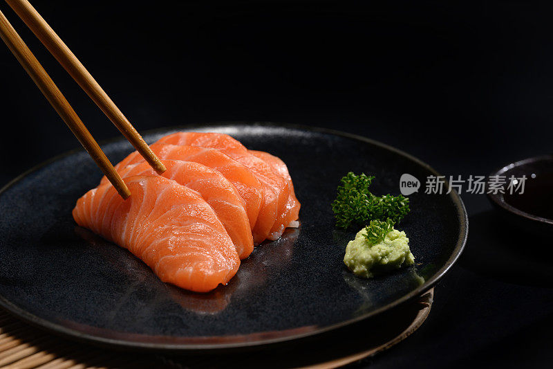 新鲜鲑鱼刺身，黑盘配山葵和欧芹叶。日式料理