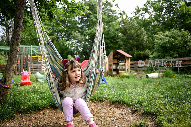 春天，小女孩在花园里的吊床上荡秋千。