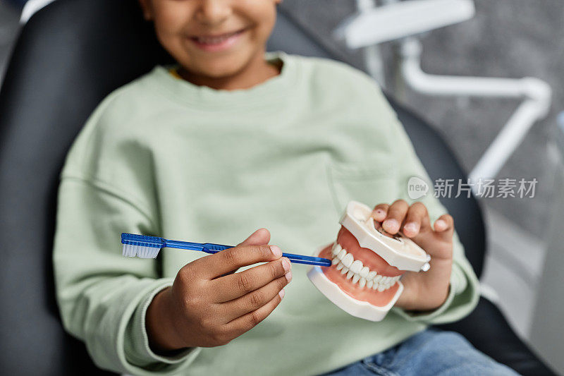 黑人小女孩在牙科椅上抱着牙齿模型的特写