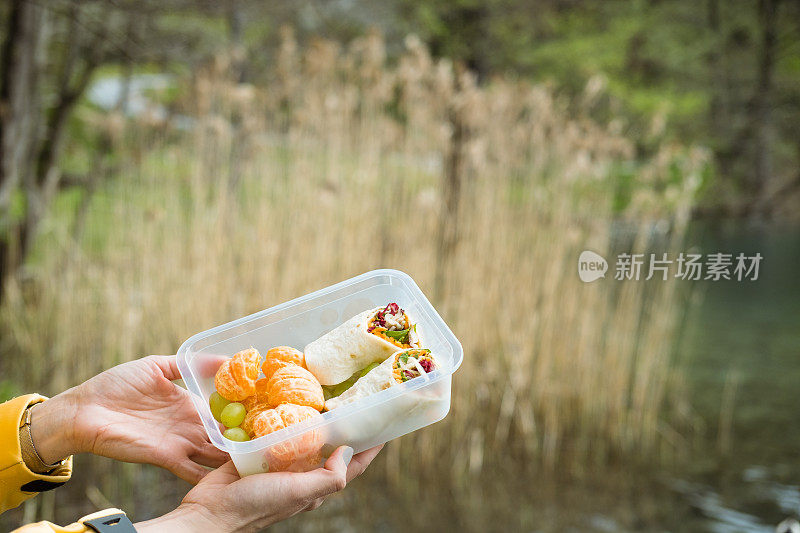 手里拿着塑料碗，里面装着玉米饼和水果。