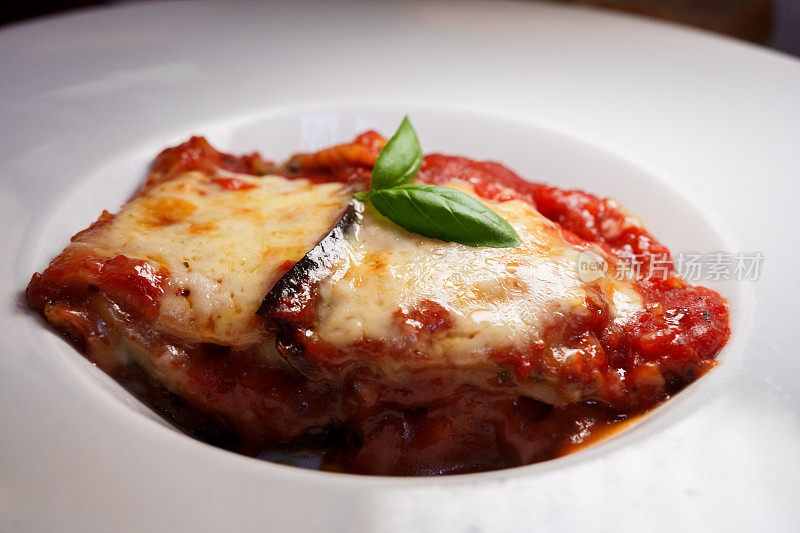 一盘美味的千层面，上面有融化的马苏里拉奶酪和一小枝罗勒和意大利番茄酱