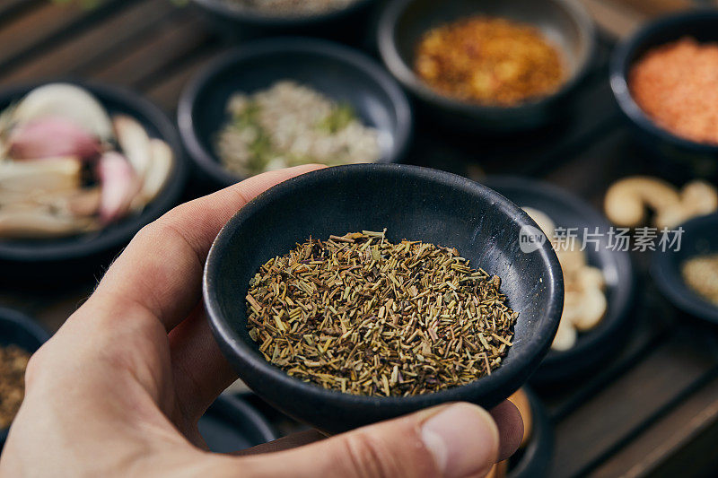 一只手拿着一个装有百里香的小陶瓷碗。用于食品制备的天然各种香料和草药