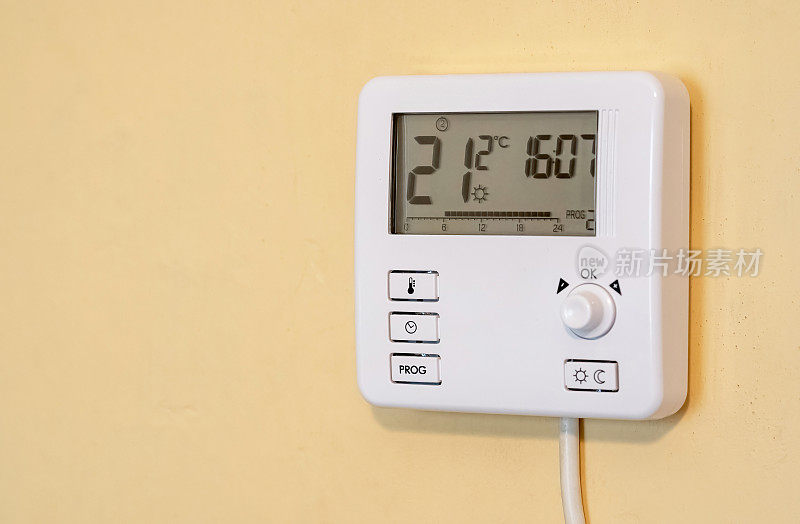 现代智能家居可编程数字恒温器单元安装在房子内的黄色墙壁上，显示当前房间温度和设置温度，在住宅公寓设置，没有人