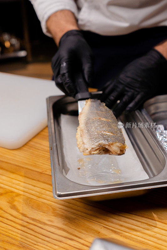 厨师戴着黑色手套的手的特写镜头，把鱼放在一个铁容器上