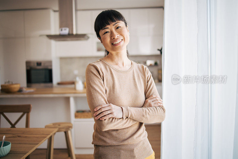 一幅日本中年妇女的肖像，微笑着站在窗后，双臂交叉。