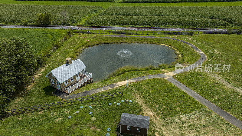 鸟瞰图:一个带喷泉的小池塘，旁边是一栋两层楼的房子和一条弯曲的小路