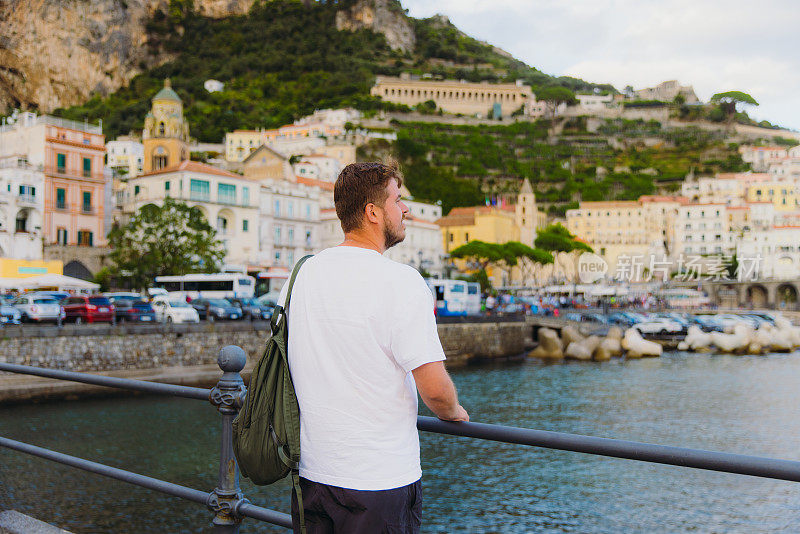 背着背包的男子在海港散步，欣赏阿马尔菲的美景