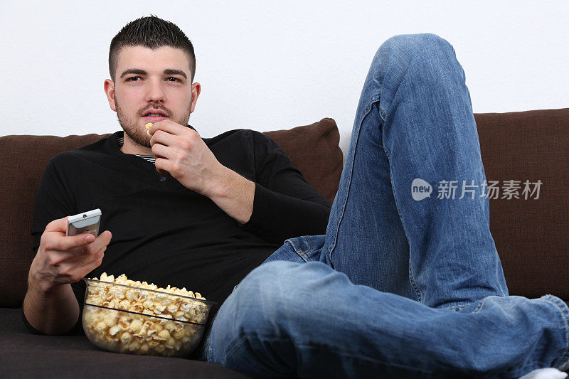 年轻人一边看电视一边吃爆米花