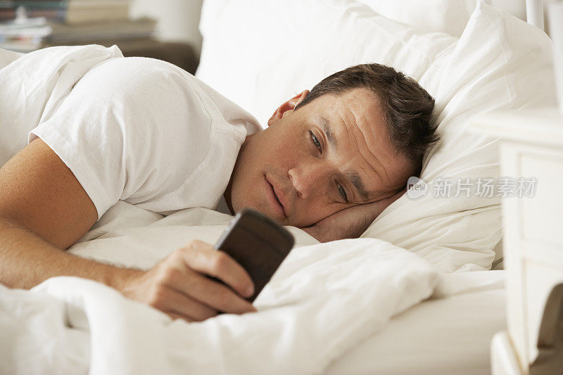 男人在家里的床上用手机发短信