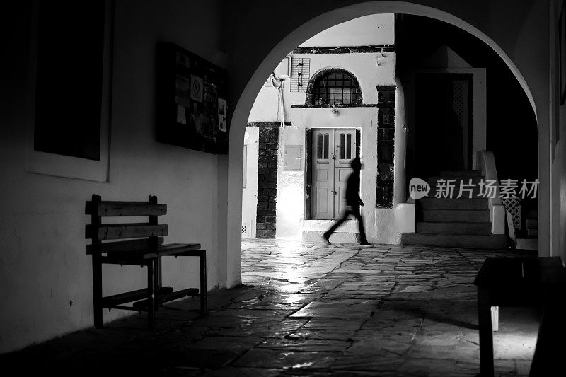 希腊圣托里尼岛伊亚镇，一名男子晚上走在一条狭窄的柏油路上的黑白照片。