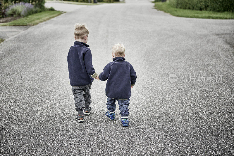 两个男孩手牵手在郊区的小街上散步