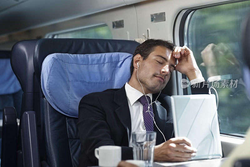 一个商人坐在火车上靠窗休息，边听音乐边休息