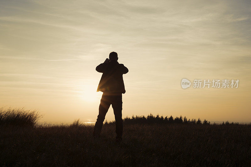 一个人站在那里用手机拍日落