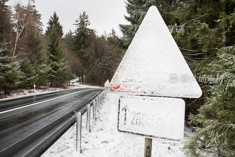 白雪覆盖的交通标志，穿过森林的道路