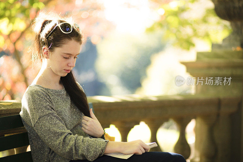 一个十几岁的女孩在秋天的公园里看书