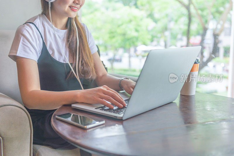 前景年轻女子坐在窗边，戴着耳机，使用笔记本电脑