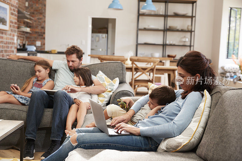 使用科技的家庭坐在开放式休息室的沙发上