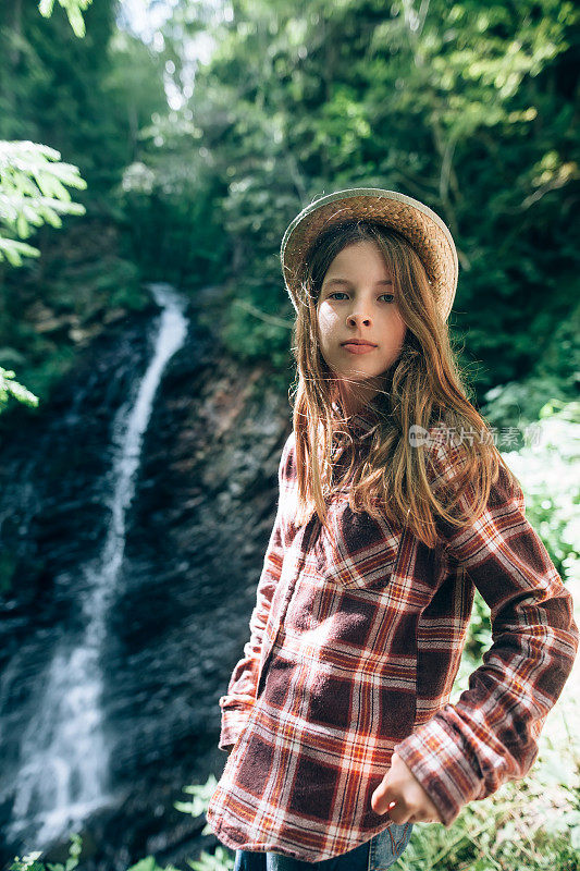 女学生穿着衬衫和草帽在瀑布背景下摆姿势