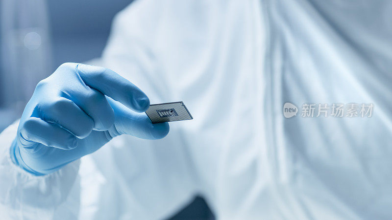 在超现代电子制造工厂，无菌工作服的设计工程师手持手套并检查微芯片。