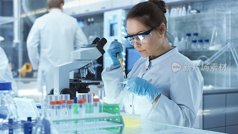 女研究科学家在一个大的现代实验室使用微型管填充试管。在背景中，科学家正在工作。