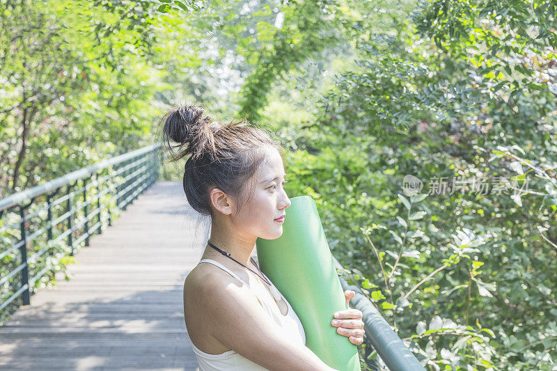 女人的肖像与瑜伽垫站在城市公园的人行天桥上