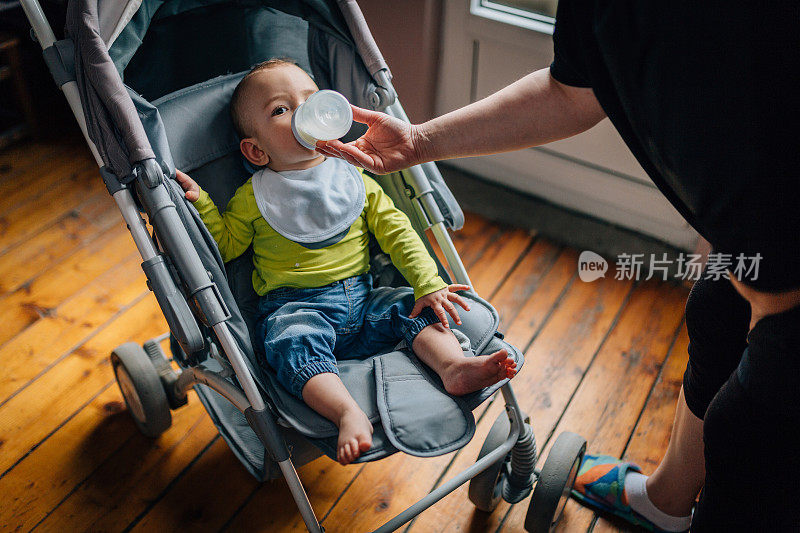 小男孩坐在婴儿车里，妈妈在给他喂奶